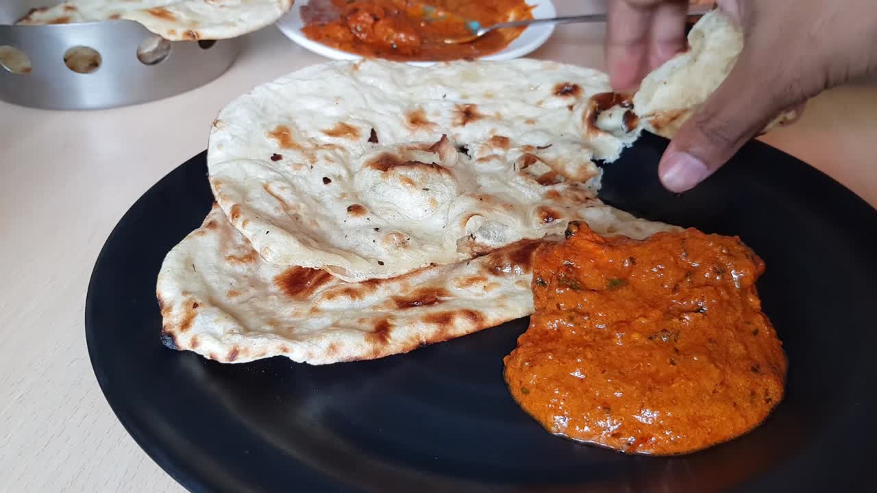 mano de un hombre indio rasgando mantequilla nan y comiendo con pollo tikka mantequilla masala de un plato negro