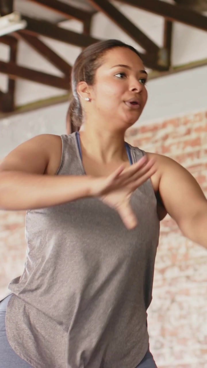 Video verticale: Donna in leggings grigi che tiene un peso al petto, eseguendo oscillazioni per la forza in studio.