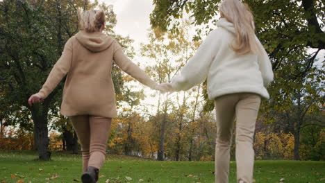 Mom-and-teenage-daughter-hold-hands-and-run-through-the-autumn-park.-Good-time-together-slow-motion-video