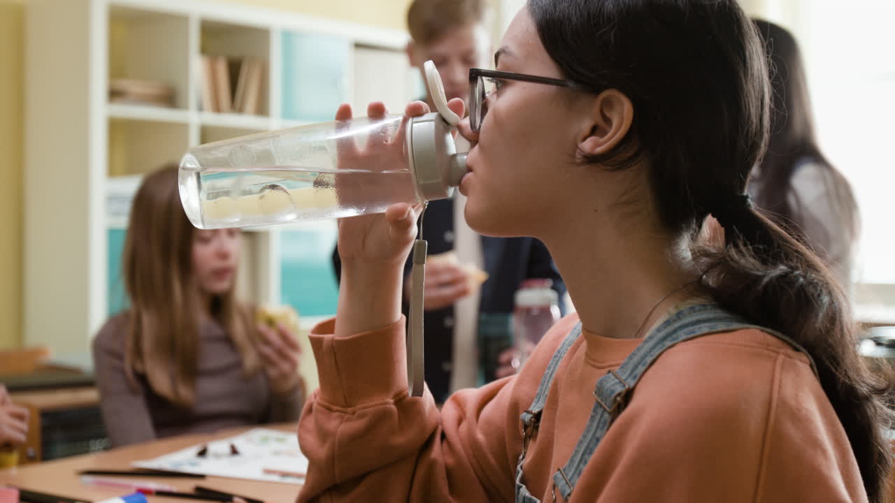 Teenage girl drinking water from a reusable bottle in a classroom