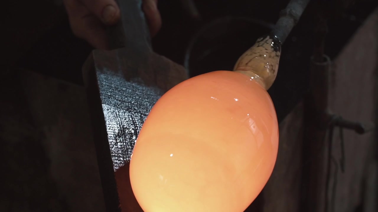 Artisan façonnant du verre en fusion incandescent dans un atelier sombre