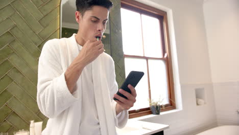 biracial man brushing teeth and using smartphone in bathroom in the morning, copy space, slow motion