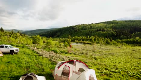 a wide view of a mountainous region is seen with tents and a white truck