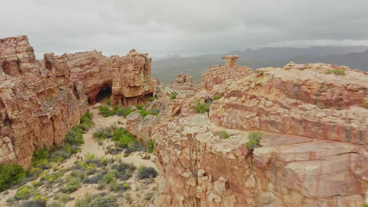 el avión no tripulado vuela lentamente más allá de formaciones rocosas en el paisaje desértico en el área silvestre de cederberg en sudáfrica - se pueden ver montañas en el fondo