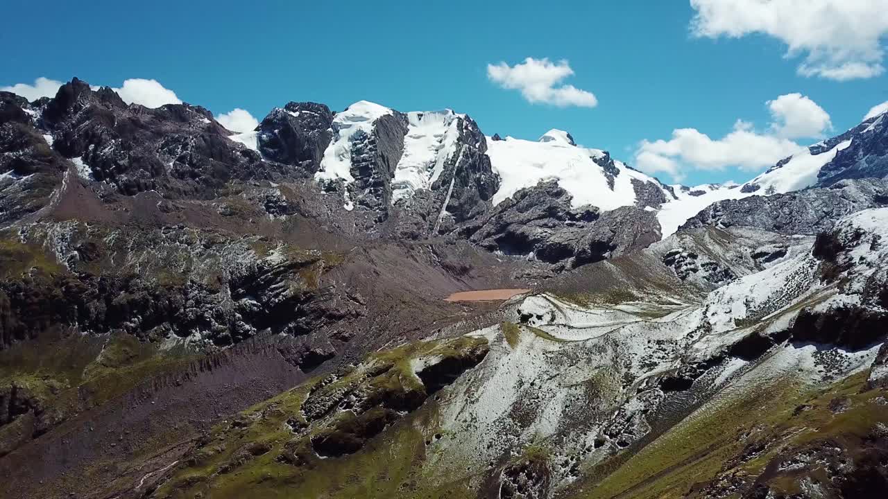 aéreo, en ascenso, disparo de drones hacia un lago marrón, en medio de picos nevados, en las montañas andinas, cielo azul, en la región de cusco, perú
