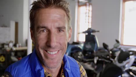 mecánico masculino mirando a la cámara en el garaje de reparación de motocicletas 4k