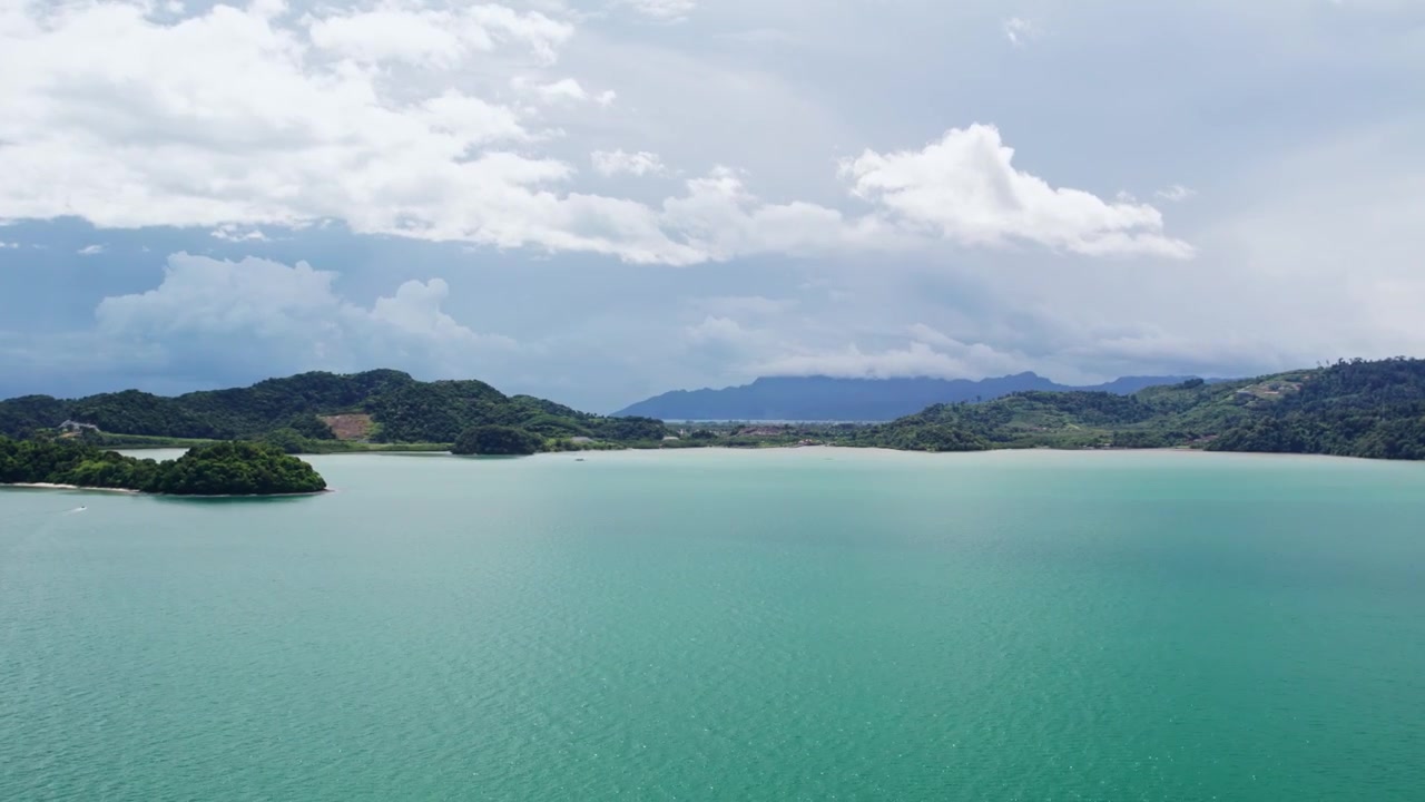 東南アジア、マレーシア。劇的な雲の下、緑豊かな森林に覆われた島々と遠くの山々に囲まれたターコイズブルーの熱帯の海の広角ドローン空撮。
