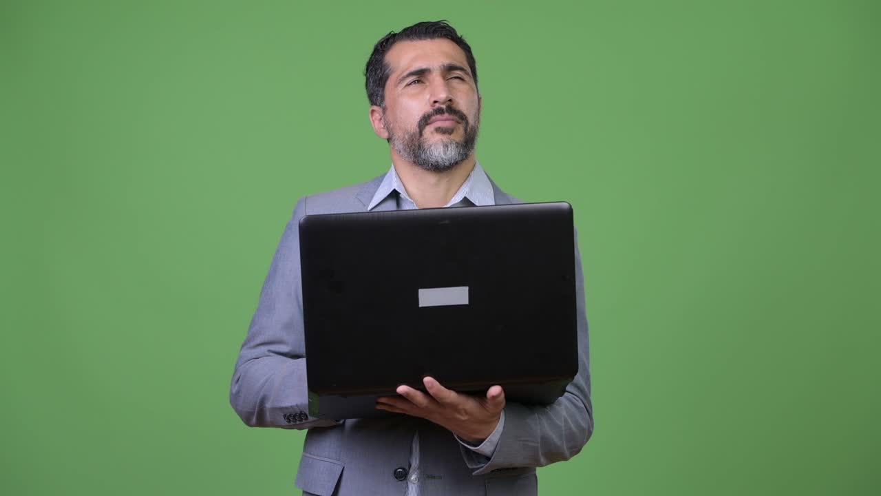 Handsome Persian bearded businessman thinking while using laptop