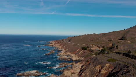 Cars-driving-down-sunny-coastal-highway-near-rocky-coast-in-Northern-California