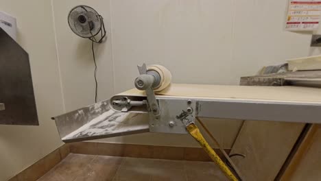 dough pin on industrial sheeter rolling up raw pizza dough.