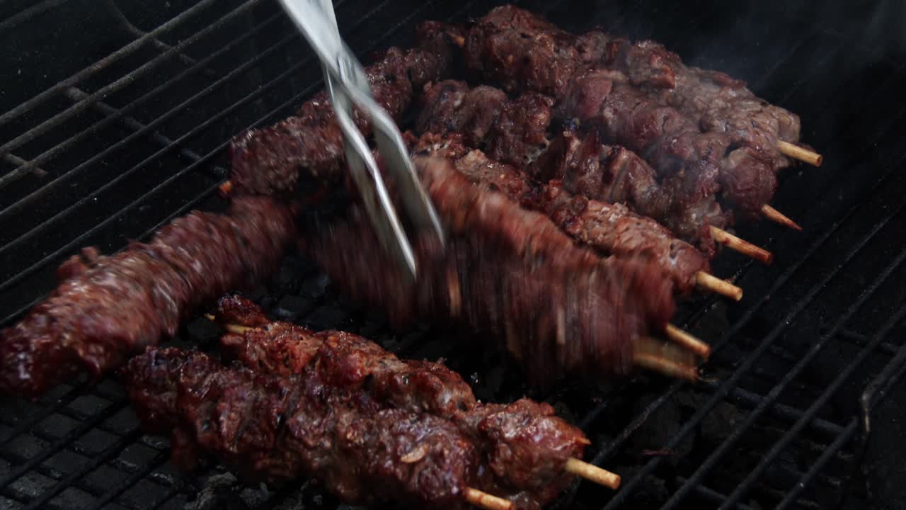 Moving juicy kebabs around the grill with tongs on a barbecue, close up