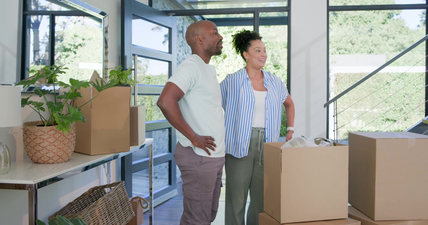 African American couple entering foyer, carrying boxes, stacking, hugging and planning move in