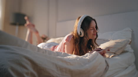 joyful girl enjoying music in earphones. carefree young woman resting bed home