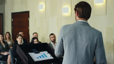 rear view of caucasian businessman speaker on a podium talking in a conference room in front to many people