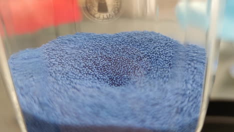 blue sand grains fall on glass clock - close up