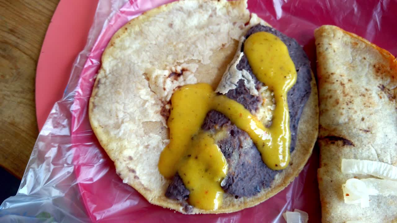 Primo piano di un taco preparato con fagioli e salsa gialla servito su un piatto rosso