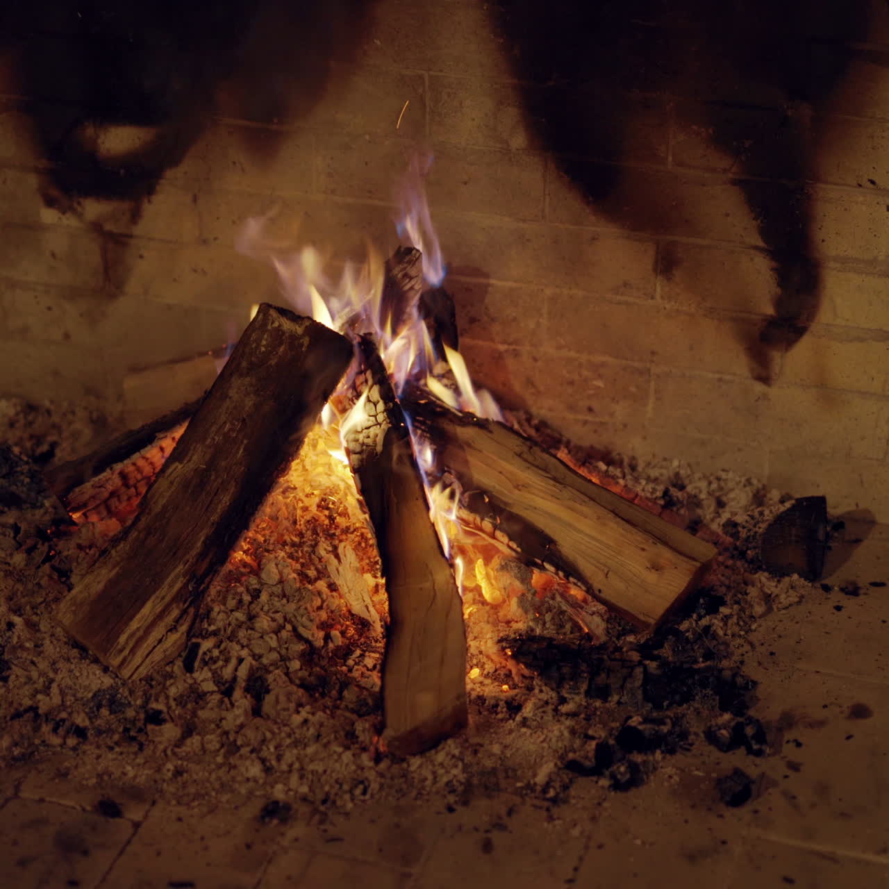 Woods burning in fireplace indoors. Sparks of bright fire woods on bricks wall background. Romantic and holiday atmosphere. Close-up.