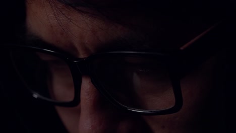 close up view of focused man wears computer glasses for reducing eye strain blurred vision looking at pc screen with computer reflection using internet, reading, watching, working online late