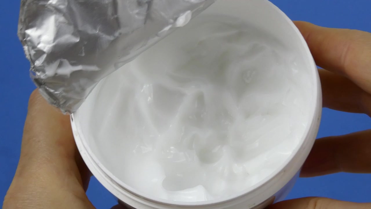 Nærbillede video af en klassisk rund krukke fyldt med skinnende hvid creme, placeret på en ren ensfarvet blå baggrund. Ideel til hudpleje, skønhed og kosmetik branding.