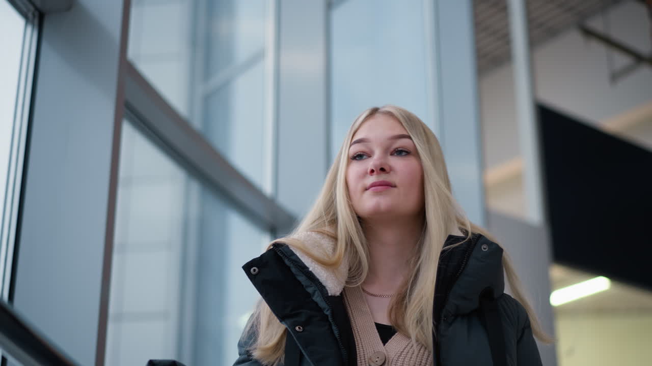 una dama sonriendo pensativa en un centro comercial moderno, rodeada de paredes de vidrio, que exuda una vibra cálida y serena, con su reflejo visible en el vidrio