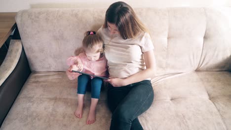 Mutter-Und-Süße-Tochter-Sitzen-Auf-Der-Couch-Und-Trainieren-Mit-Einem-Tablet-Computer.-Tochter-Denkt-Nach