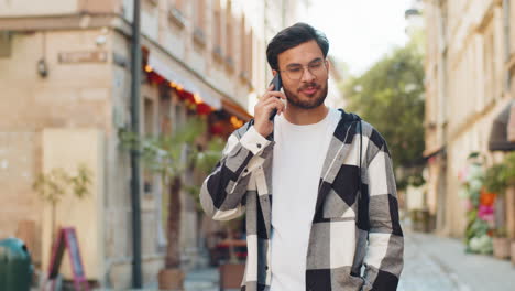 indian young man tourist on smartphone chatting with friend while walking in the city street