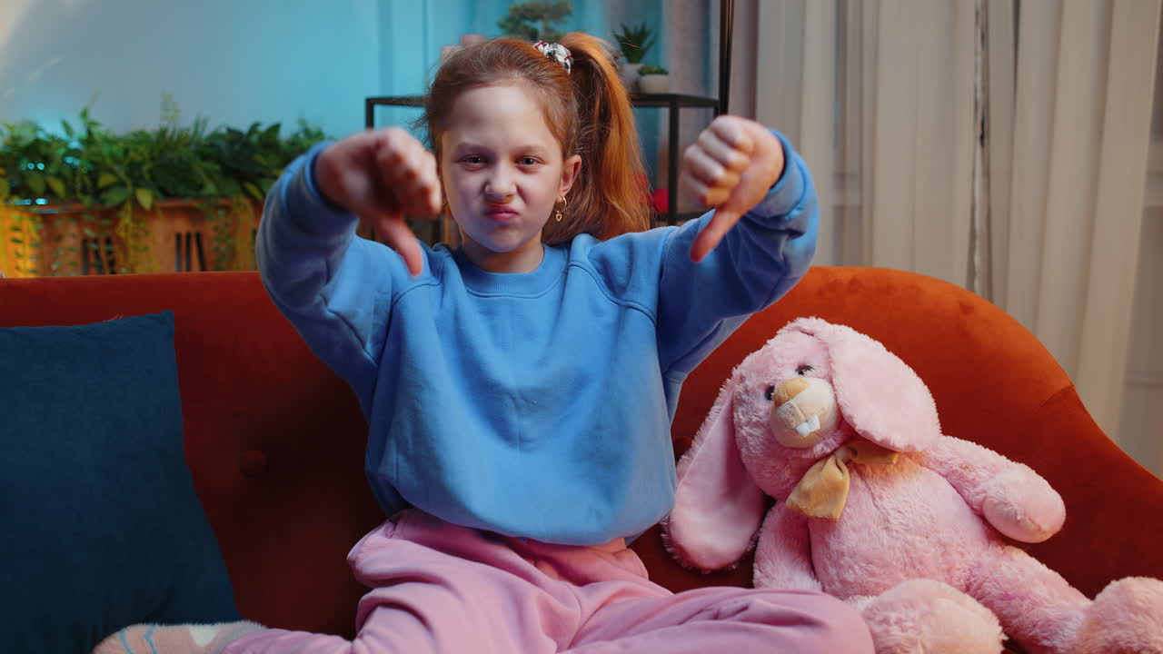 Upset teen girl showing thumbs down dislike bad work disapproval dissatisfied feedback at home