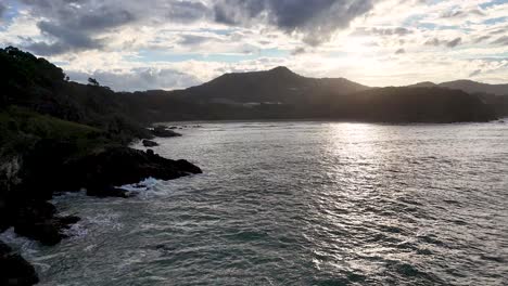 A serene sunset over Charlesworth Bay with gentle waves and lush greenery, captured in soft, natural lighting