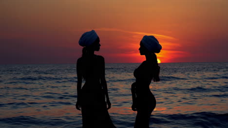 silhouettes of two women wearing turbans at sunset by the ocean