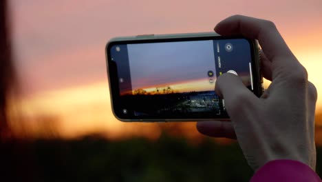 una mujer usando su teléfono para capturar un cielo rojo y el sol poniéndose