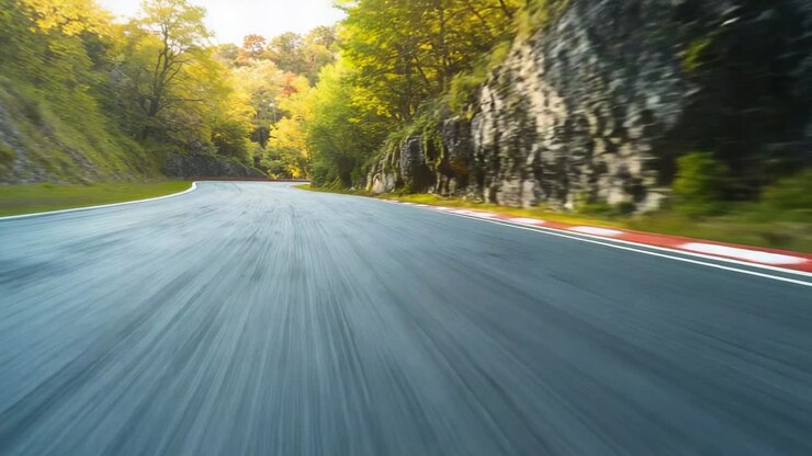 Propelling camera rolling over asphalt along canyon road, with red-white curb showing autumn forest