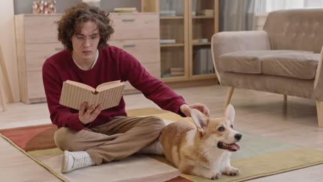 man reading book and petting corgi