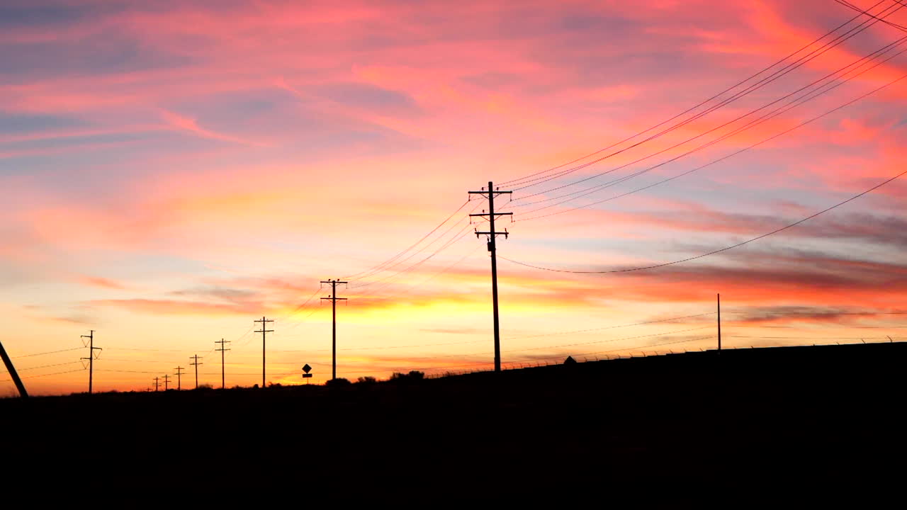 A colorful sunrise sky looking down a country road in the USA with telephone poles and electric wires in silhouette vanishing into the distance