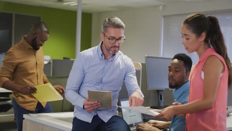 Diverse-male-and-female-business-colleagues-using-tablet-and-talking-in-office