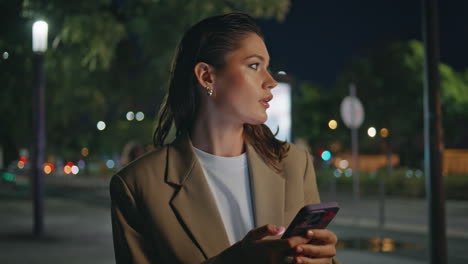 mujer caminando buscando teléfono celular en la calle de noche cerca. chica yendo a casa tarde