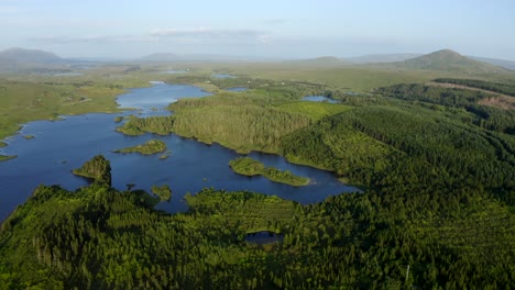 ballynahinch lake, recess, connemara, county galway, ireland, july 2021. drone slowly tracks south over woods and islands with the garraun mountain complex, ballinafad and maam in the distance