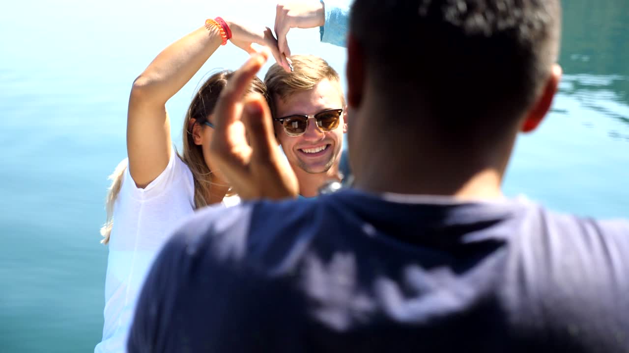 pareja feliz sentada en la proa del barco y posando en la cámara en un día soleado. fotógrafo ayudando a la pareja joven a tomar una posición correcta para la foto en la cubierta del barco. concepto de vacaciones o vacaciones.