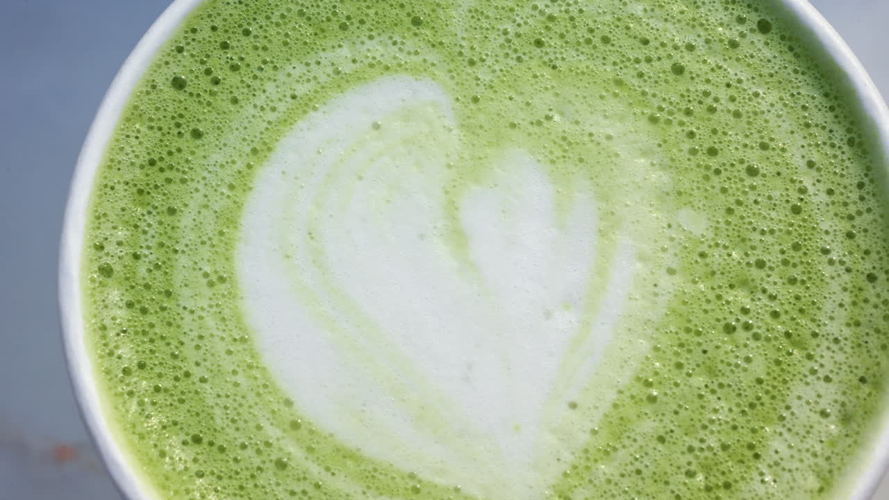 Vista superior em close-up de um latte matcha verde com arte latte em forma de coração num copo para viagem