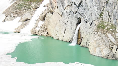 fresh alpine melted water falls from hole in rock of swiss alps into turquoise glacial lake