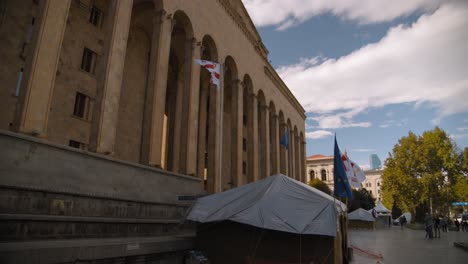tbilisi, georgia parliament building with waving flags, clouds and blue sky.