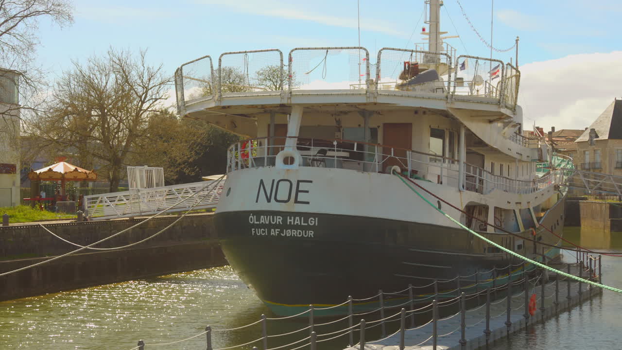 A large white ship is docked in a canal in Rochefort, France, on a sunny day with calm waters