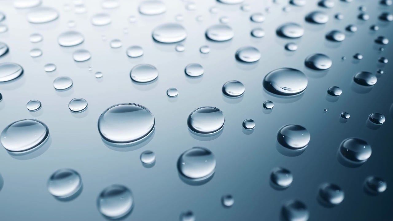 Macro view of scattered water droplets on a smooth reflective plane. Larger droplets sit in the foreground with smaller beads receding toward the upper right