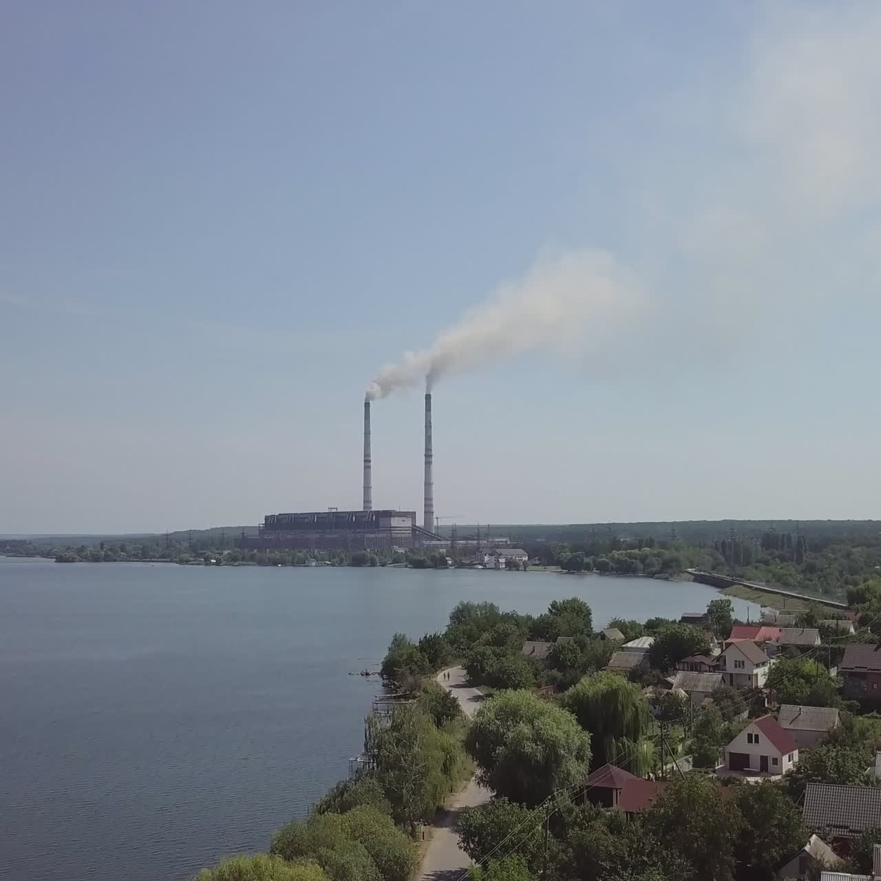 Beautiful view of the village and the river, surrounded by nature from the birds-eye view. Big power plant with pipes in the center of the village. Aerial view