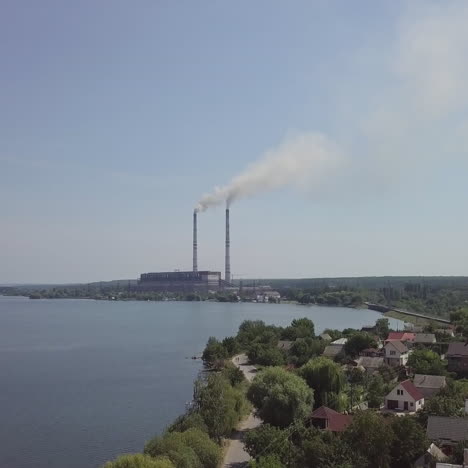beautiful view of the village and the river, surrounded by nature from the birds-eye view. big power plant with pipes in the center of the village. aerial view
