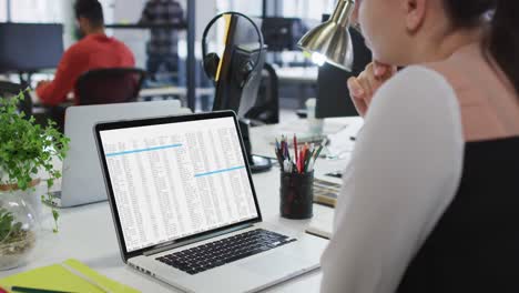 mujer caucásica sentada en un escritorio viendo el procesamiento de datos de codificación en la pantalla de una computadora portátil