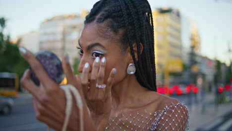 model applying makeup at evening street closeup. woman looking mirror