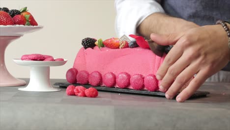 Close-up-of-chef's-hands-cutting-cake-with-strawberry-topping