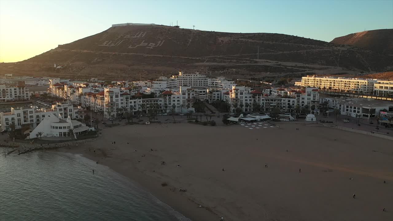 Aerial view of Agadir beach and city with mountain backdrop at sunset, Morocco
