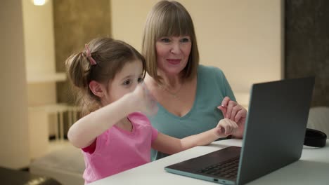 Portrait-of-nice-granny-and-grandchild-using-laptop-making-video-calls-waving-hi-hello