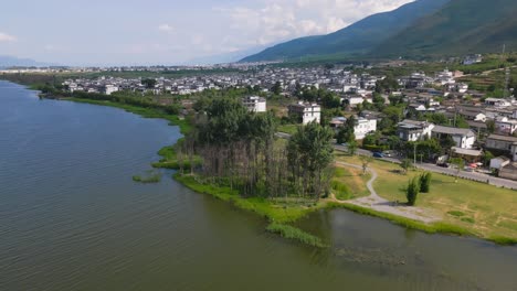 Die-Drohnenaufnahmen-Schwenken-über-Die-Straße-Entlang-Einer-Kleinen-Dorfsiedlung-In-Er-Hai-Und-Führen-Weiter-Zum-Ruhigen-Und-Berühmten-See-In-Der-Bergregion-Von-Dali-In-Der-Provinz-Yunnan,-China